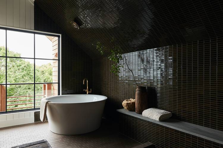 Alt-Text: „Modernes Badezimmer mit dunklen Fliesen, einer freistehenden Badewanne, großem Fenster und Holzbank; illustriert hochwertige Sanitärtechnik, Energieeffizienz und ästhetische Raumgestaltung.