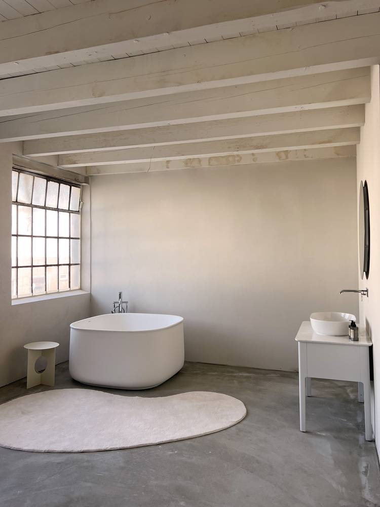 Alt-Text: „Modernes Badezimmer mit freistehender Badewanne, integriertem Wandwaschbecken und Sichtbalken in einem energieeffizienten Gebäude, optimal für SHK-Fachplaner und Facility Manager.“.