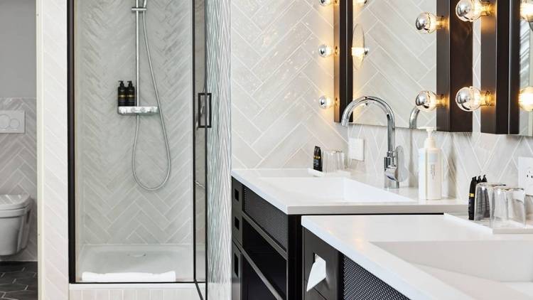 Alt-Text: „Modernes Badezimmer mit barrierefreier Glasdusche, doppelten Waschtischen, beleuchteten Spiegeln und energieeffizienten LED-Leuchten – Ideal für zeitgemäße Gebäudetechnik-Lösungen.