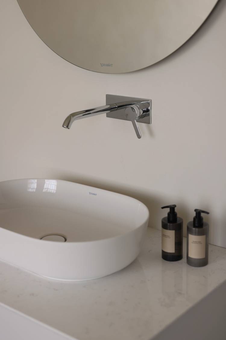 ALT-Text: „Stilvolles Badezimmer mit runder Spiegeloberfläche, energieeffizientem Wasserhahn und zwei umweltfreundlichen Seifenspendern auf einer Marmorarbeitsplatte, repräsentiert nachhaltige Sanitärausstattung für moderne Gebäude.“.