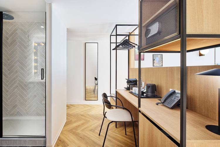 ALT-Text: „Hochmodernes Hotelzimmer mit Fokus auf energieeffiziente Gebäudetechnik; ausgestattet mit intelligenter Beleuchtung, digitalem Thermostat für Heizungssteuerung, raumoptimiertem Arbeitsplatz und barrierefrei zugänglicher Glas-Duschkabine.