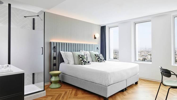 ALT-Text: „Hotelzimmer mit energieeffizientem Heizsystem, bodengleicher barrierefreier Dusche und Stadtblick; ideale Lösungen für moderne Gebäudeplanung in der Gebäudetechnikbranche.