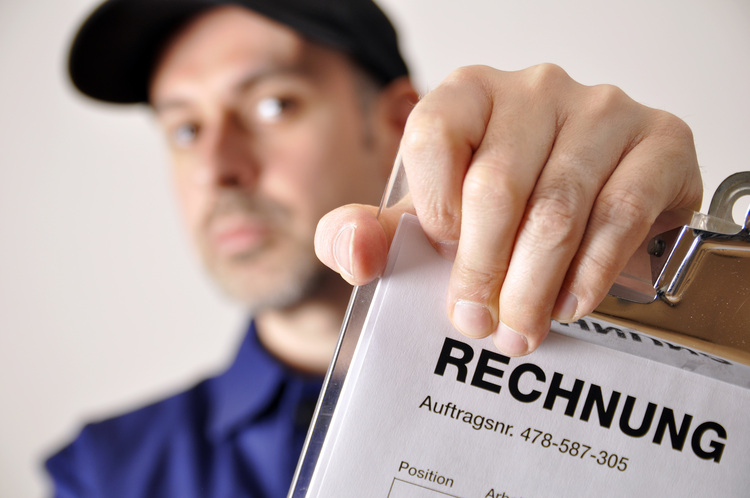 ALT-Text: „Fachkundiger Gebäudetechniker in blauer Arbeitskleidung überprüft eine Rechnungsübersicht, um die Energieeffizienzmaßnahmen eines Gebäudes zu evaluieren.