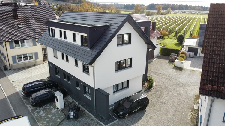 ALT-Text: „Energieeffizientes Gebäude mit moderner Heizungs-, Lüftungs- und Klimatechnik, umgeben von nachhaltigen Umgebungen wie Bäumen und einem Weinberg, symbolisiert fortschrittliche Gebäudetechnologien für Entscheider.