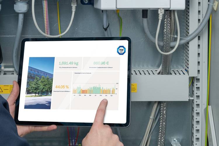 ALT-Text: „Facility Manager überprüft Umwelt- und Energiedaten auf einem Tablet in einem Heizungsraum mit moderner Gebäudeleittechnik.
