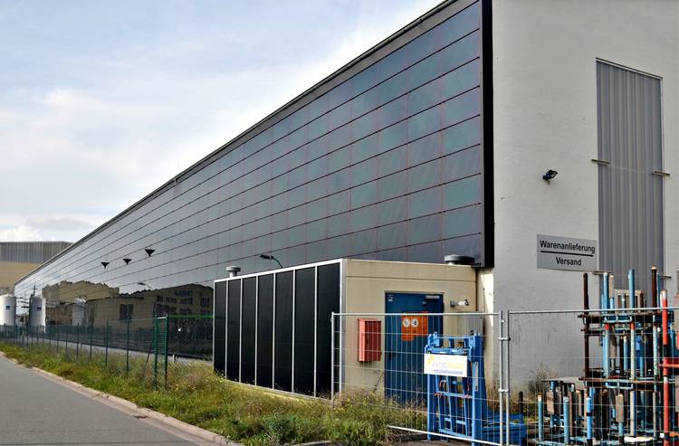 ALT-Text: „Industriegebäude mit Dach-Solaranlagen und abgeschirmtem Bereich, der komplexe Rohrleitungen für Heizungs-, Lüftungs- und Klimatechnik zeigt.
