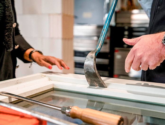Zwei Fachhandwerker montieren mithilfe von Spezialwerkzeugen einen Glasrahmen auf einem Arbeitstisch in einer Werkstatt für Sanitär- und Gebäudetechnik.