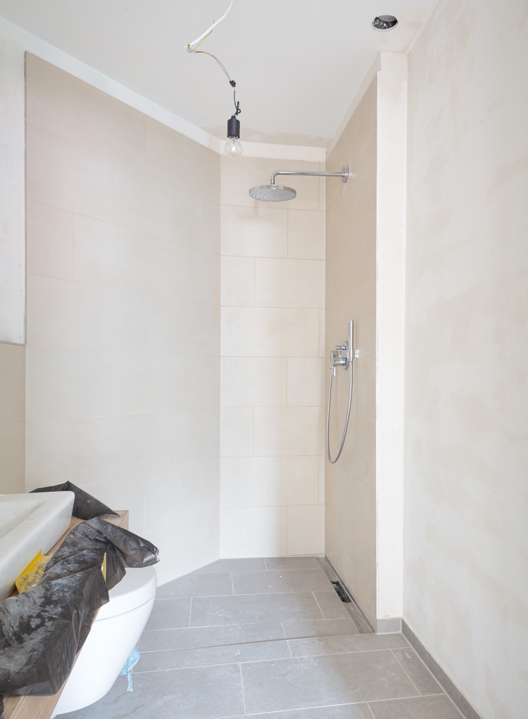 ALT-Text: „Sanierung eines barrierefreien Badezimmers mit rahmenloser Dusche, rutschfesten beigefarbenen Fliesen und optimierter Beleuchtung für energieeffiziente Gebäudetechnik.