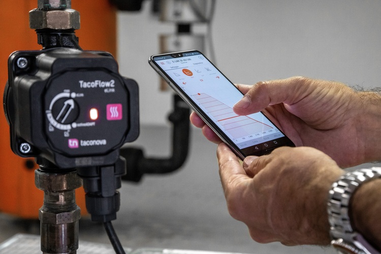 Alt-Text: „Fachkraft konfiguriert über Smartphone die TacoFlow2-Pumpe in einer komplexen Gebäudetechnikinstallation.