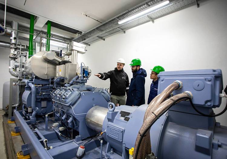 ALT-Text: „Drei Fachleute in Schutzhelmen begutachten eine industrielle HVAC-Anlage in einem Fabrikumfeld für energieeffiziente Modernisierung.