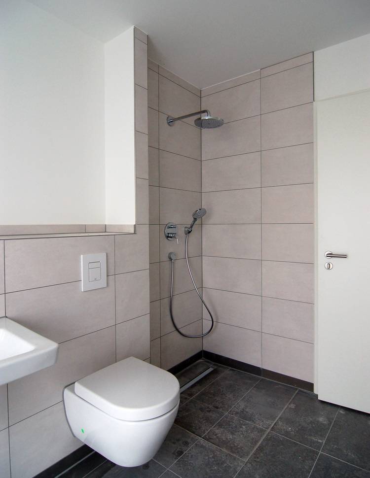 Barrierefreies Badezimmer mit wandhängendem WC und ebenerdiger Dusche, ausgestattet mit rutschfesten grauen Fliesen und modernem Design – optimal für SHK-Planung in der Gebäudetechnik.