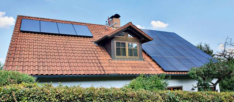 Selbstversorgendes Wohngebäude mit rotem Ziegeldach und integrierten Solarmodulen, umgeben von nachhaltiger Landschaftsgestaltung, symbolisiert moderne Ansätze zur Energieeffizienz und Nutzung erneuerbarer Energien in der Gebäudetechnik.