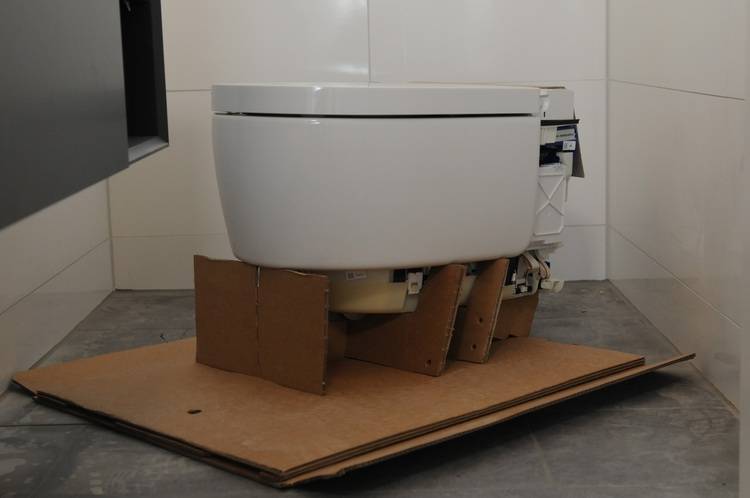 ALT-Text: „Teilweise installierte moderne Toilettenschüssel auf Kartonplatten in einem gefliesten Badezimmer, bereit für den Anschluss an nachhaltige Sanitärsysteme im Rahmen energieeffizienter Gebäudetechniklösungen.“.