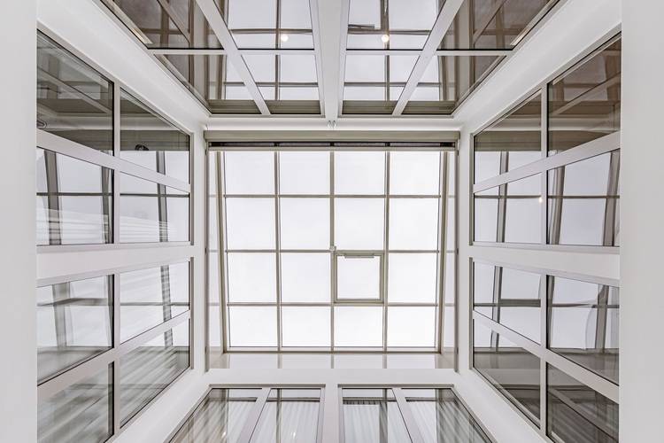 Alt-Text: „Blick nach oben auf das moderne Glasatrium eines energieeffizienten Bürogebäudes, unterstützt von tragenden Metallträgern und Fenstern, die ein geometrisches Raster bilden und Tageslichtnutzung in der Gebäudetechnik veranschaulichen.