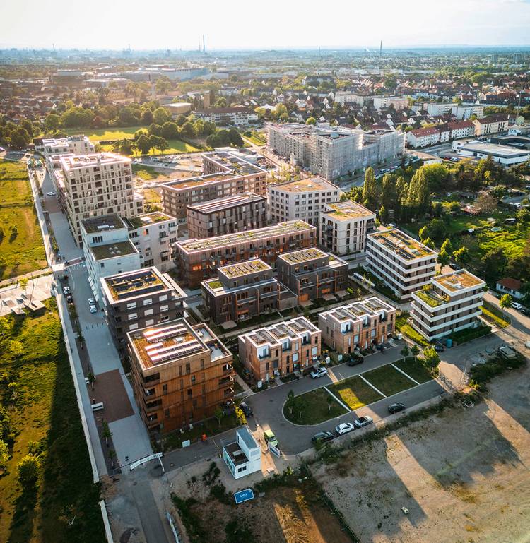 Alt-Text: „Luftaufnahme eines modernen Wohnkomplexes mit energieeffizienter Gebäudetechnik, umgeben von grünen Freiflächen und städtischer Infrastruktur im Hintergrund.