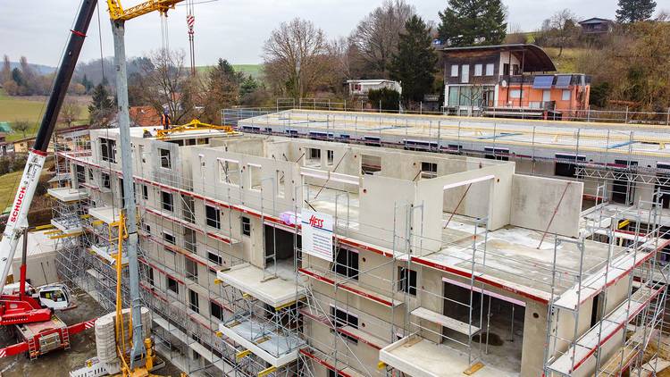 Alt-Text: "Blick auf eine Baustelle für ein nachhaltiges Mehrfamilienhaus mit fortschrittlicher Gebäudetechnik; Kräne heben Bauteile, während das neueste Heizungs- und Lüftungssystem installiert wird, um Energieeffizienz zu maximieren.