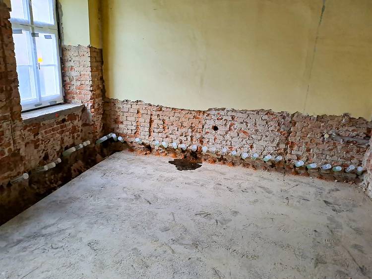 ALT-Text: „Raum in Sanierung mit freigelegten Ziegelwänden, Fenster und sichtbaren Installationsrohren für Sanitär- und Heiztechnik – perfekt zur Veranschaulichung bautechnischer Modernisierungsprozesse für Entscheider in der Gebäudetechnik.