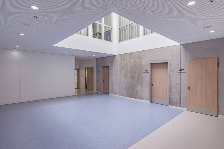 Alt-Text: „Moderner Flur in einem Bürogebäude mit energieeffizienter LED-Beleuchtung, blauer rutschfester Bodenbelag für Sicherheit und Schallschutzwände zur Verbesserung der Raumakustik, nummerierte Holztüren bieten Zugang zu multifunktionalen Besprechungsräumen.