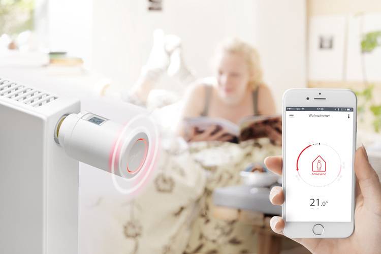 Alt-Text: „Ein Branchenexperte steuert ein intelligentes Heizkörperthermostat über eine Smartphone-App in einem modernen Wohnraum zur Optimierung der Energieeffizienz.