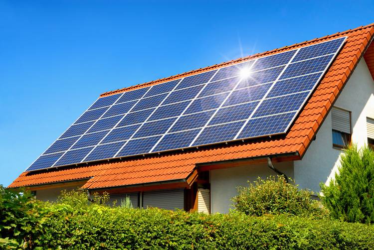 Alt-Text: „Ein modernes Gebäude mit rotem Ziegeldach, ausgestattet mit Photovoltaikanlage zur Nutzung erneuerbarer Energien, symbolisch für energieeffiziente Gebäudetechnik unter klarem Himmel.“.