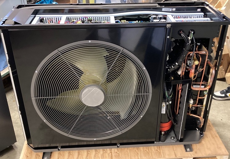 Alt-Text: "Seitenansicht einer industriellen Klimaanlage mit freigelegten internen Komponenten und großem Lüfter, illustriert die Komplexität moderner Gebäude-Lüftungssysteme für TGA-Spezialisten und Entscheidungsträger.