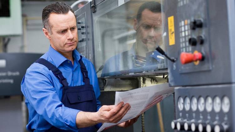 Alt-Text: „Fachhandwerker in blauer Arbeitskleidung überprüft eine Heizungsanlage und notiert technische Daten für die Gebäudeeffizienz.