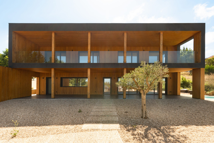 ALT-Text: „Energieeffizientes zweistöckiges Holzhaus mit großen Fenstern und Schotterlandschaft, das moderne architektonische Ansätze für nachhaltige Gebäudetechnik und optimierte Energienutzung präsentiert.“.