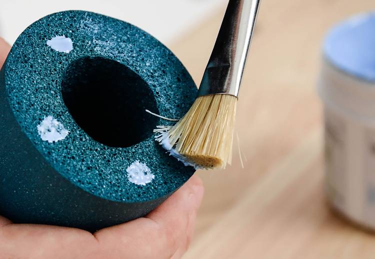 Alt-Text: „Detailaufnahme eines Facharbeiters, der einen Klebstoff mit einem Pinsel auf einen blauen Isolierschaumzylinder aufträgt, um Schall- und Wärmedämmung in Heizungsinstallationen zu gewährleisten.“.