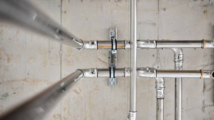 Alt-Text: „Installierte Metallrohre und Armaturen auf einer Betonwand, die ein komplexes Netzwerk für Sanitär-, Heizungs- und Klimatechnik in einem modernen Gebäude darstellen.