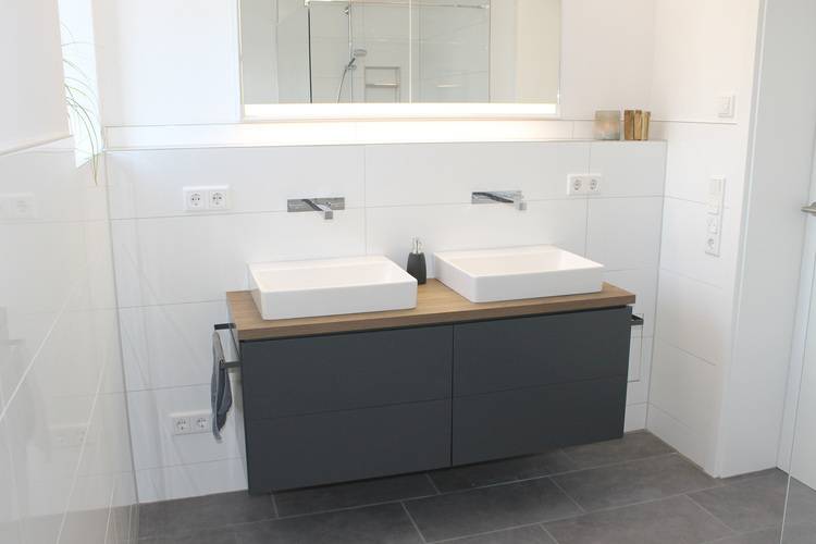 Alt-Text: „Modernes Badezimmer mit doppeltem Waschbecken, wandmontierten Armaturen, dunklem schwebendem Waschtischunterschrank und großem Spiegel – ideal für energieeffiziente Gebäude im SHK-Bereich.