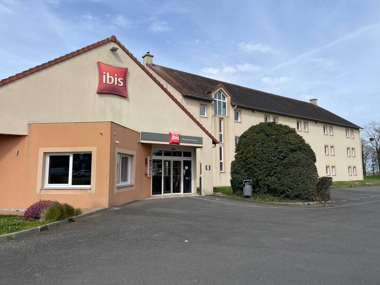 ALT-Text: „Barrierefreier Hoteleingang mit automatischer Tür und ebenerdigem Zugang, beige Fassade, gepflegte Grünanlagen und großzügiger Parkplatz unter klarem Himmel – optimale Infrastruktur für barrierefreies Gebäudedesign in der Hotellerie.