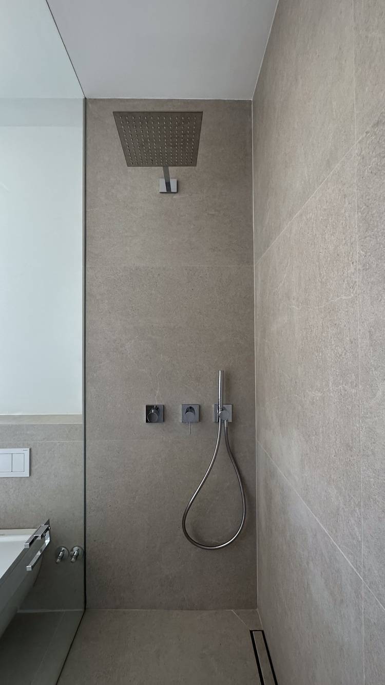 Barrierefreie Duschlösung mit modernem Regenduschkopf und Handbrause, eingebaut in beige gefliesten Wänden für optimale Zugänglichkeit im Sanitärbereich.
