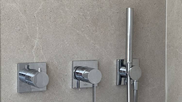 Alt-Text: „Moderne, einstellbare Duscharmaturen und Handbrause mit wassersparender Technologie an einer beige gefliesten Wand, ideal für nachhaltige SHK-Lösungen.