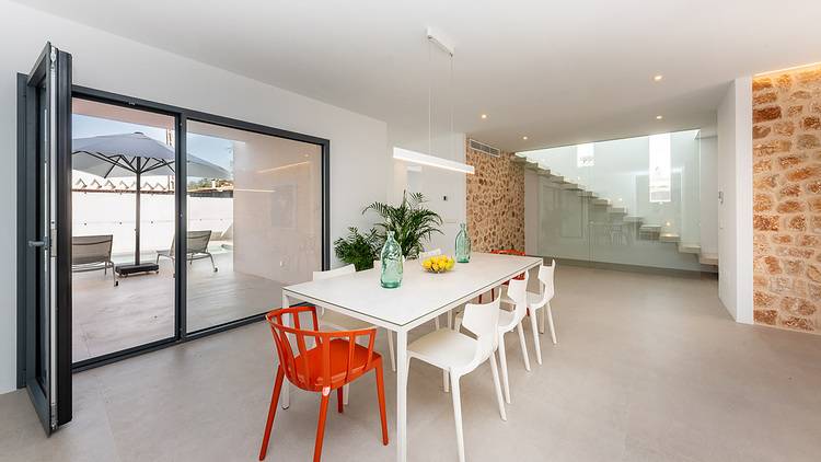 Alt-Text: „Moderner Besprechungsraum im Gebäude mit gläserner Schiebetür, weißem Konferenztisch, verschiedenen Sitzgelegenheiten und angrenzender Treppe, die zu einem sonnigen Außenbereich mit Liegestühlen führt. Ideal für Gebäudetechniklösungen zur Verbesserung der Energieeffizienz und Nutzung natürlicher Lichtquellen.