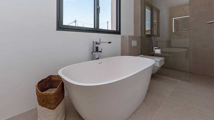 ALT-Text: „Modernes Badezimmer mit freistehender Badewanne, ideal für energieeffiziente Renovierungen in der Gebäudetechnikbranche, inklusive nachhaltiger Materialien wie einem Korb aus Naturfasern und großem Fenster zur Optimierung des natürlichen Lichteinfalls.“.