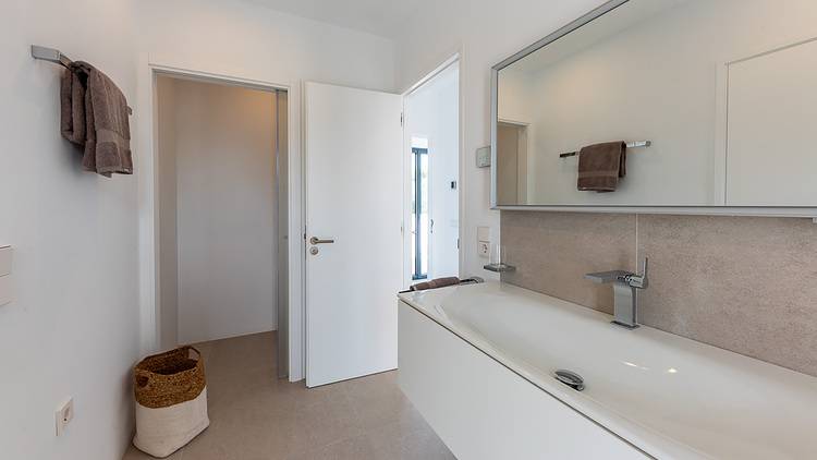 Alt-Text: „Moderner Sanitärraum mit freistehender weißer Badewanne, großem spiegelndem Wandpanel zur Verbesserung der Energieeffizienz, offenem Türrahmen für barrierefreien Zugang und Handtuchhalterung samt nachhaltigem Aufbewahrungskorb aus Naturmaterialien.“.