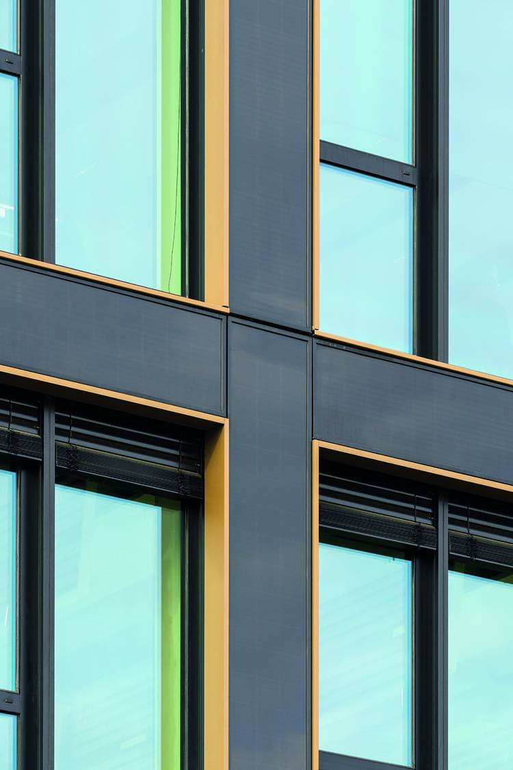 ALT-Text: Detailansicht einer modernen Gebäudefassade mit großen Glasfenstern und auffälligen gelb-schwarzen Vertikallinien, die innovative Architektur und energieeffiziente Bauweise in der Gebäudetechnikbranche veranschaulichen.