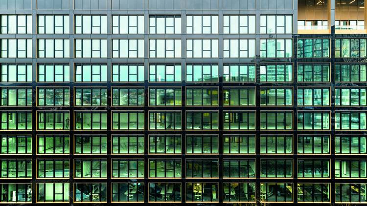 Alt-Text: „Moderne Gebäudeoberfläche mit symmetrischen, grün getönten Fenstern, die Energieeffizienz und innovative Dämmmaterialien in der Gebäudetechnik hervorheben.“.