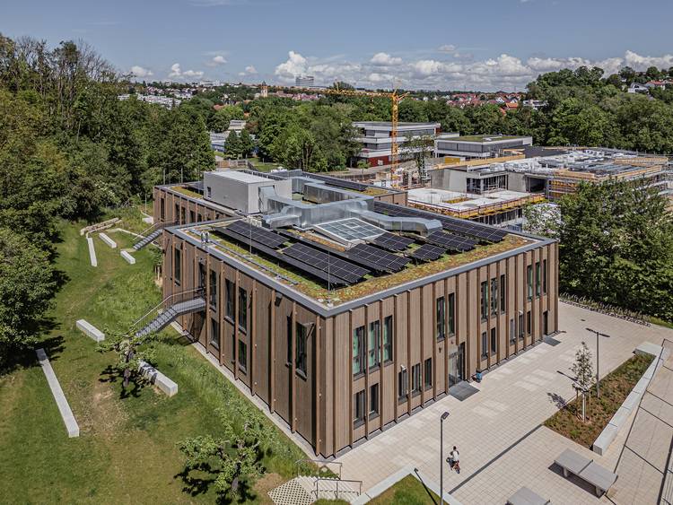 Vogelperspektive eines modernen Bürogebäudes mit Solaranlagen auf einem begrünten Dach, umgeben von weiteren Gebäuden und Bäumen, symbolisiert nachhaltige Bauweise und Energieeffizienz in der Gebäudetechnik.