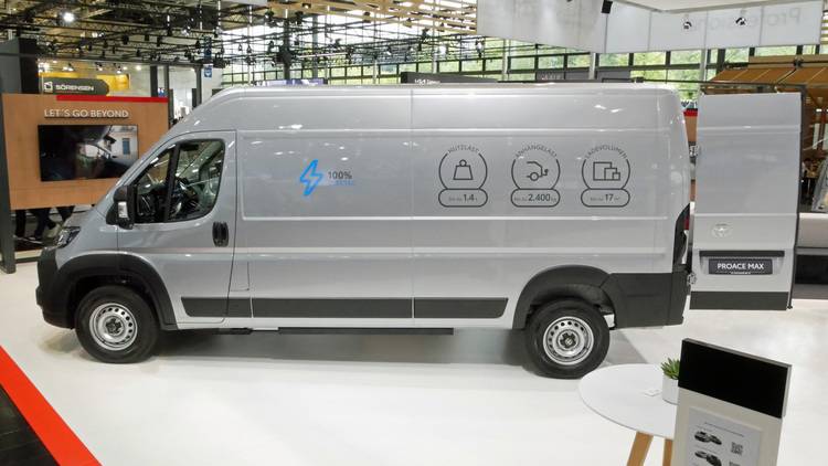 ALT-Text: „Silberner Proace Max Elektro-Van in Innenausstellung mit Symbolen für Energieeffizienz auf der Seite, hervorgehoben als zukunftsweisende Lösung für nachhaltige Mobilität in der Gebäudetechnikbranche.“.