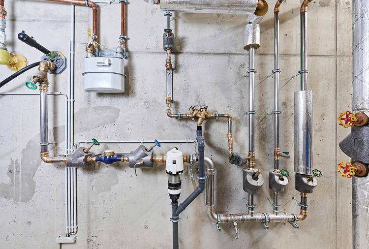 „Detailaufnahme eines komplexen Sanitär- und Heizungssystems in einem Technikraum: Verrohrung und Ventile für energieeffiziente Gebäudeinstallation.