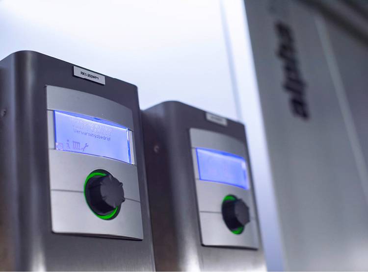 Alt-Text: „Zwei digitale Regelgeräte zur Steuerung von Heizungs- und Klimasystemen, an einer Wand montiert, im modernen Industriedesign mit blauer LED-Anzeige für präzise Temperaturregelung in Gebäudeautomationsanwendungen.