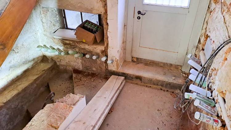 Ein funktionales Technikraumdesign mit robuster Steintreppe, gelagerten Sanitärkomponenten und einer Tür zur Wärmeversorgungseinheit.