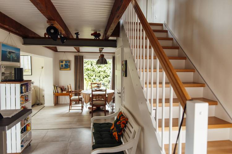 Innenansicht eines energieeffizienten Wohnraums mit maßgefertigtem Heizsystem, moderner Holztreppe und Platz für nachhaltige Sanitärinstallation. Der Blick auf den Garten dient als Beispiel für ganzheitliche Gebäudetechniklösungen im Einklang mit erneuerbarer Energie.