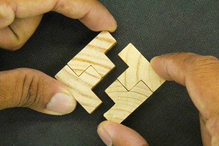 Zwei Hände halten ineinandergreifende Holzteile eines Puzzles vor einem dunklen Hintergrund, symbolisierend die Integration nachhaltiger Energielösungen in der modernen Gebäudetechnik.