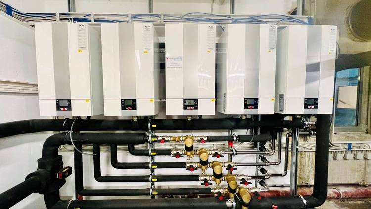 Industrie-Brennwert-Wassererhitzer mit schwarzen Rohrleitungen und gelben Absperrventilen in einem Technikraum zur Optimierung der Energieeffizienz in gewerblichen Gebäuden.