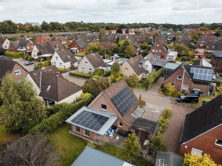 Luftaufnahme eines Wohngebiets mit zahlreichen Einfamilienhäusern, grünen Bäumen und mehreren Dächern, die mit Solaranlagen ausgestattet sind; symbolisiert die Integration erneuerbarer Energien in moderne Gebäudetechnik für erhöhte Energieeffizienz.