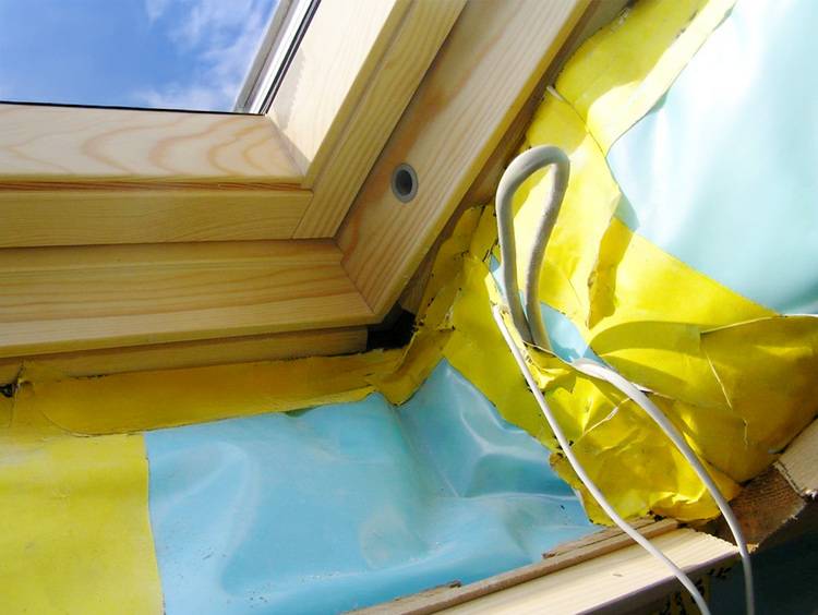 Innenansicht eines Dachfensters mit gelbem und blauem Dämmmaterial zur Verbesserung der Energieeffizienz, sichtbarem Kabel für elektrische Anschlüsse in der Gebäudetechnik.