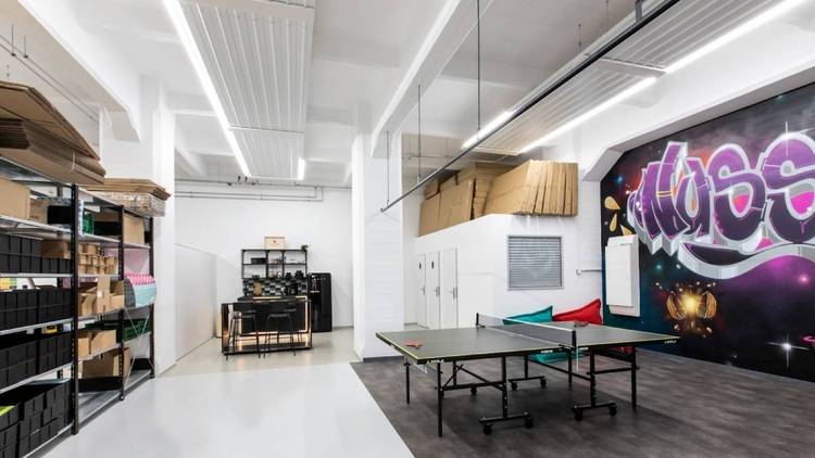 ALT-Text: „Moderner Besprechungsraum mit integriertem multifunktionalem Freizeitbereich, ausgestattet mit Tischtennistisch für Teambuilding, modularen Regalsystemen für Anlagenpläne, künstlerischen Wandgrafiken zur ästhetischen Aufwertung und flexibler Sitzgruppe für informelle Meetings in der Gebäudetechnikbranche.“.