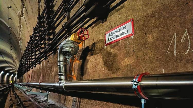 Alt-Text: „Blick in einen Versorgungstunnel einer Industrieanlage, ausgestattet mit diversen Rohrleitungen und einem gut sichtbaren roten Ventil an der Wand. Ein Sicherheitsschild markiert die Entnahmestelle für Löschwasser – ein zentraler Aspekt der Anlagensicherheit in modernen Gebäudetechniksystemen.“.